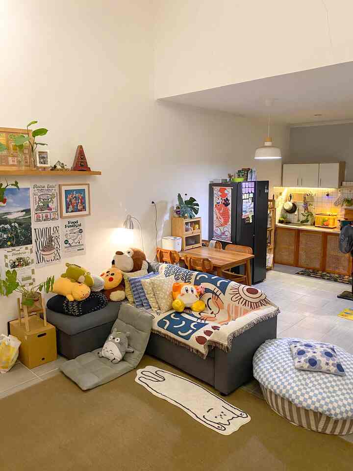 Natural-toned open living room and kitchen featuring a sofa bed, bean bag, various cushions, and posters in a warm cozy atmosphere