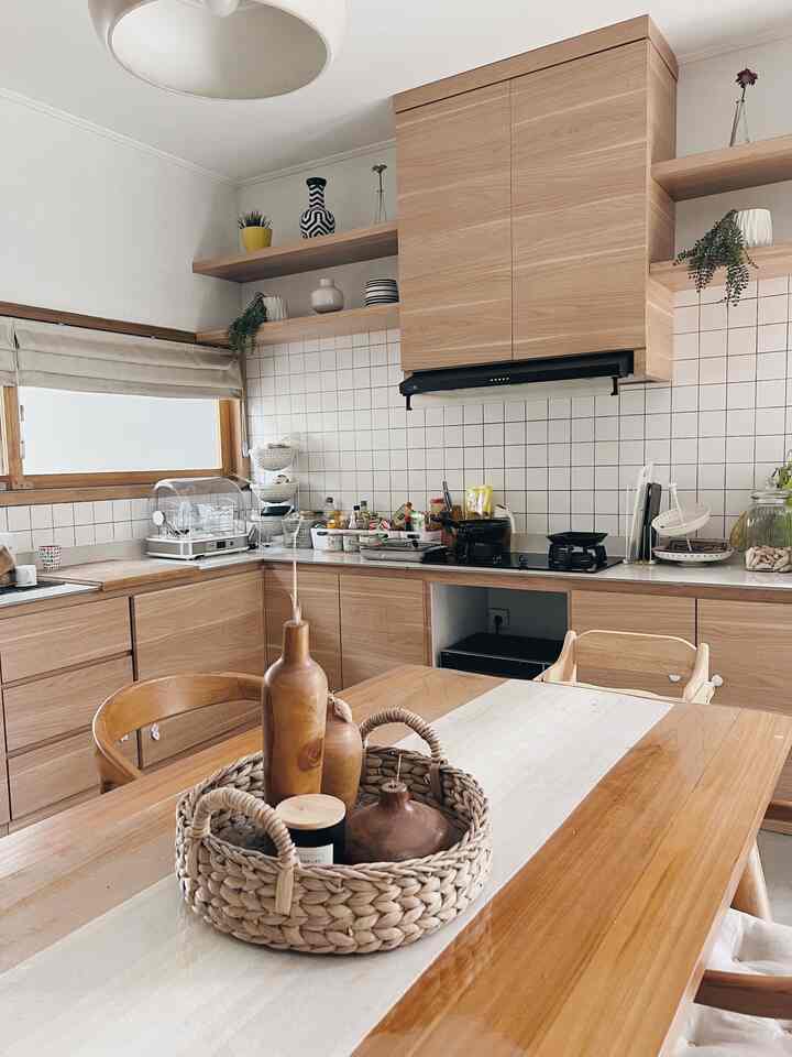 Compact kitchen featuring natural wood tones and white tiled backsplash, with cabinetry and dining table creating a warm atmosphere