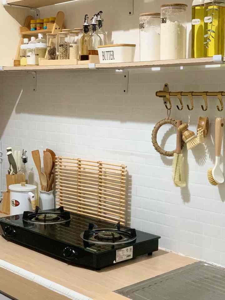 White tiled backsplash with wood-toned shelves and a black gas stove in a kitchen space
