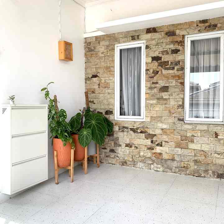 White and yellow natural stone wall, simple white shoe cabinet, and green plants arranged in a bright, clean entrance space