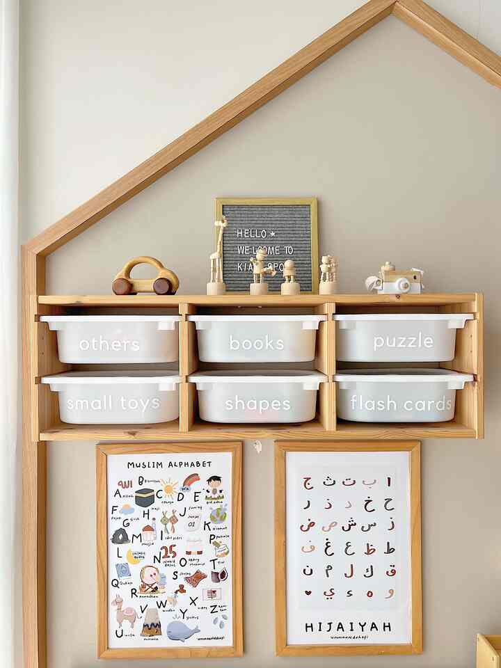 Natural-toned kids' room with beige wall, wooden shelves holding white storage bins and framed children's educational posters