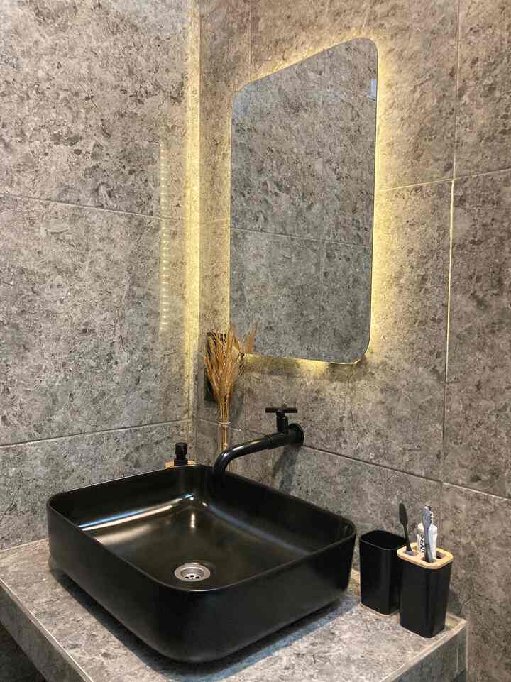 Modern industrial bathroom with black wash basin, LED-lit mirror, and gray stone tiled walls