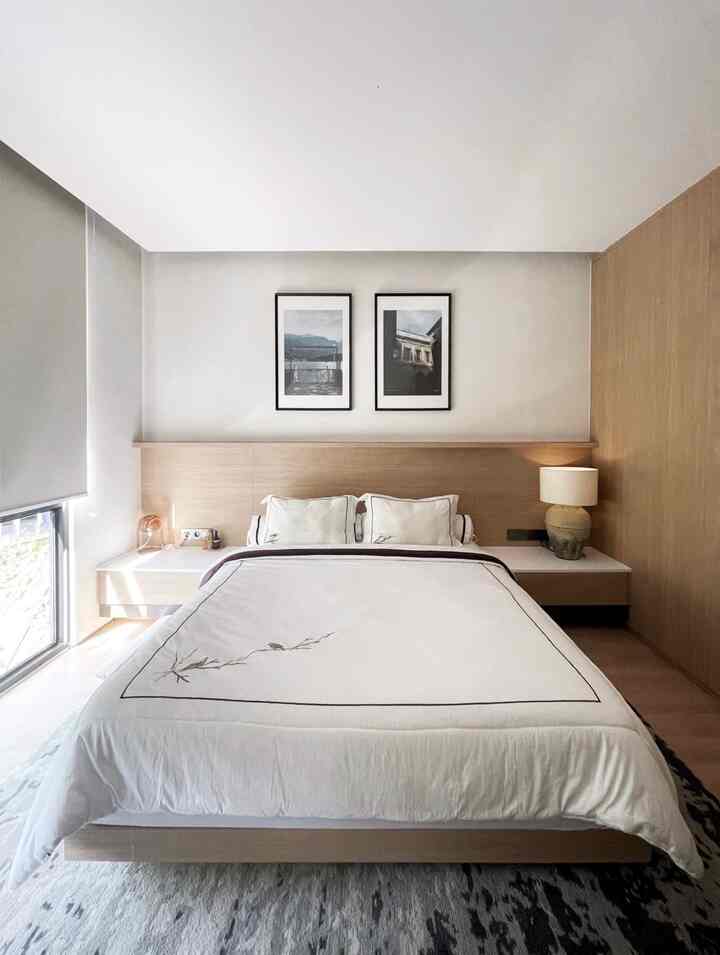 A simple modern bedroom in white and wood tone featuring a centrally placed bed with storage cabinets on both sides, creating a restful space