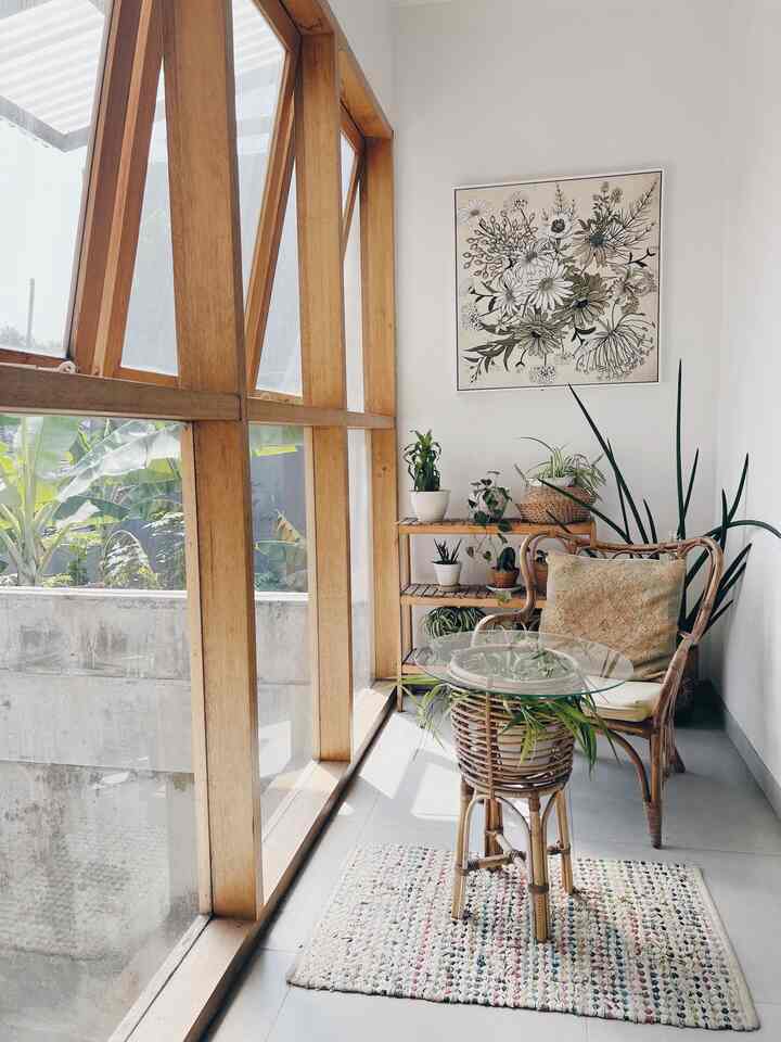 Natural toned hallway space featuring a rattan armchair, glass table, and multiple plants with a simple design