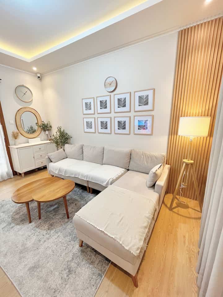 Japandi style living room with natural wood tones and white walls, featuring beige sofa and warm floor lamp creating a cozy atmosphere