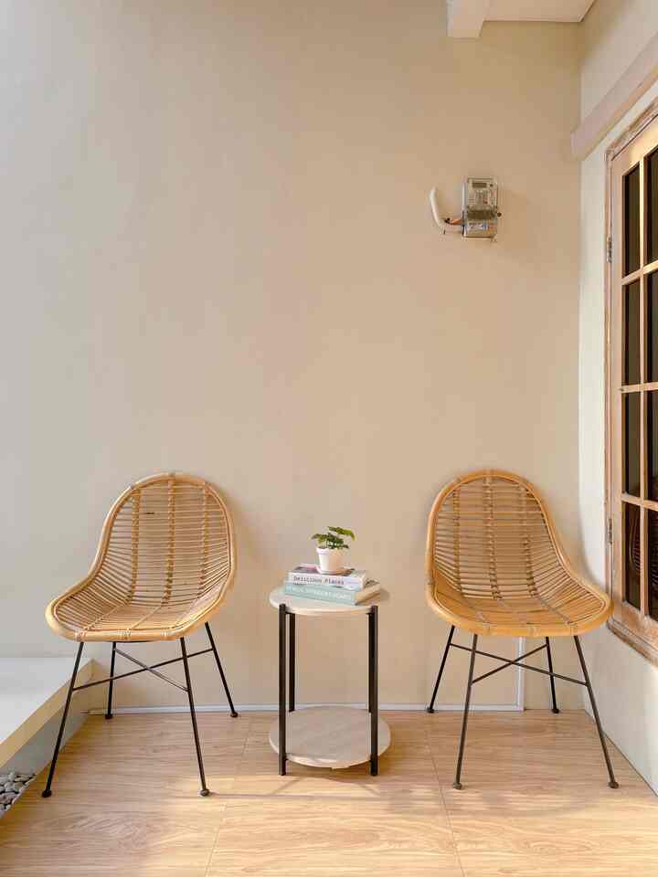 Beige wall and wood-tone floor balcony featuring two rattan chairs and a small round side table with a calm, natural atmosphere