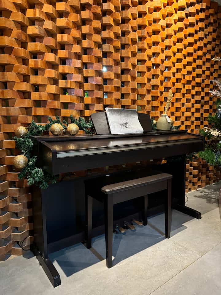 Music space featuring black digital piano against brown brick wall with Christmas garland decor
