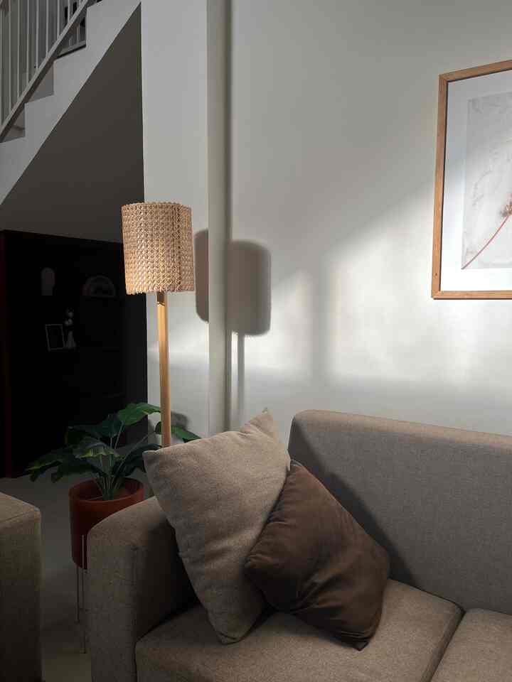Natural beige-toned living room featuring a beige sofa with brown cushions and a rattan floor lamp illuminated by warm golden hour sunlight