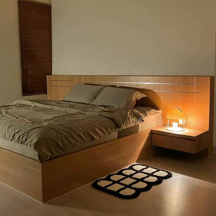 Natural wood tone and beige bedroom featuring bed and nightstand with warm lighting creating cozy atmosphere