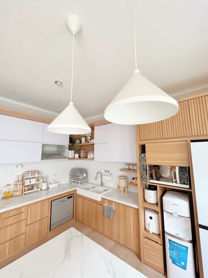 White and wood tone kitchen space featuring clean cabinetry, pendant lights, and electronic appliances in a cozy Japandi style interior