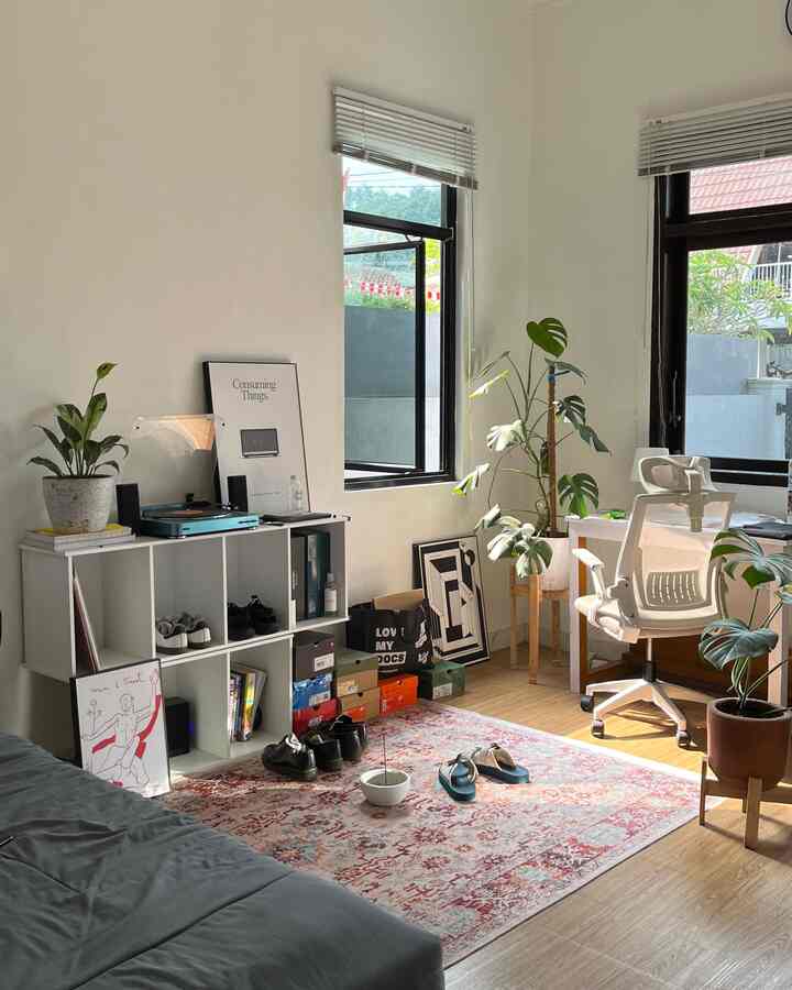 White walls and wood tone flooring in a single household home office space featuring desk, chair, shelving units, and multiple plants creating a cozy atmosphere