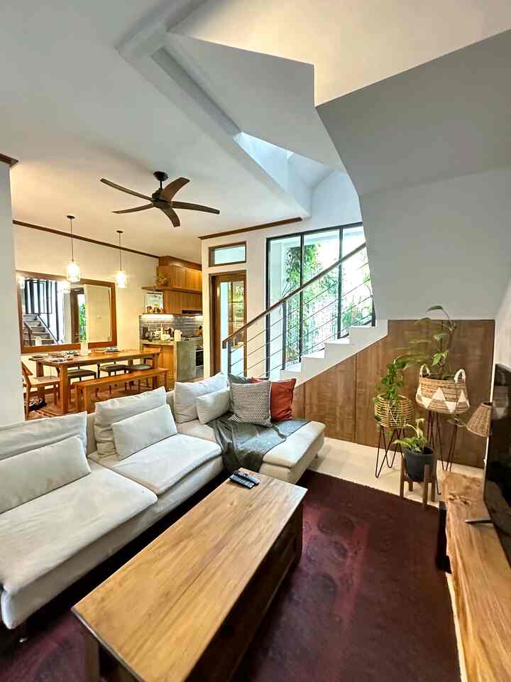 Bright white living room featuring a large sofa, wooden furniture, and a maroon carpet creating a cozy atmosphere