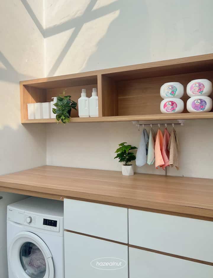 Natural wood shelves and countertop in a long narrow white laundry space, featuring organized storage and plants for a clean interior