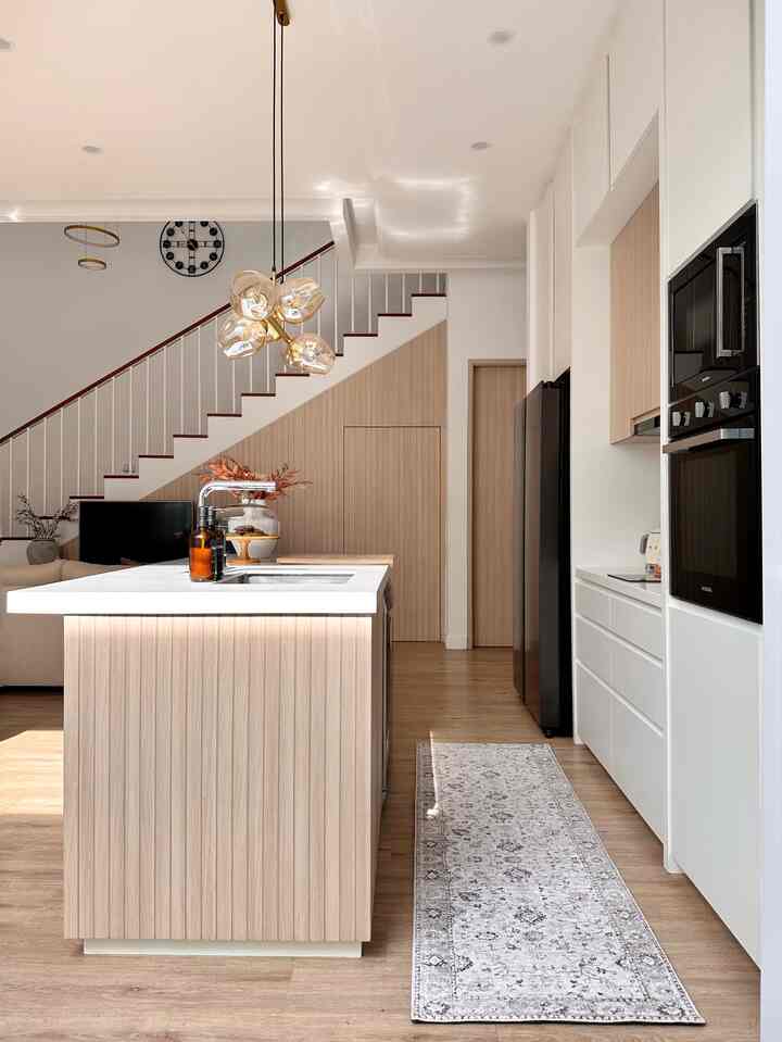 Natural wood tones with white in a kitchen space featuring a central kitchen island and stairs, presenting a clean modern interior