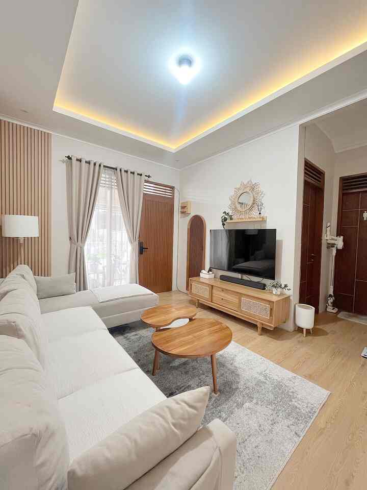 Natural wood tones and white hues blend in this living room featuring a large sofa, round coffee tables, and a TV stand creating cozy atmosphere