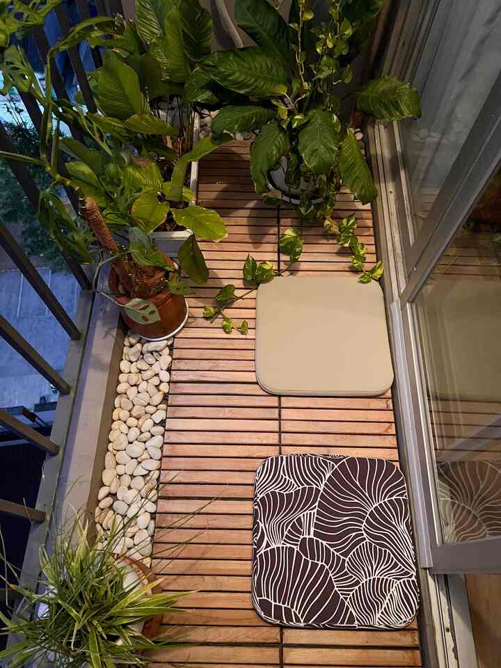 Wood tone balcony space featuring beige and patterned seat cushions on floor with lush green plants, creating a cozy atmosphere