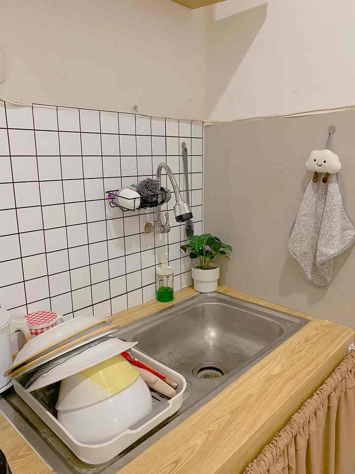 Natural wood-tone kitchen sink area with white tiled wall and organized kitchen items, compact and practical space