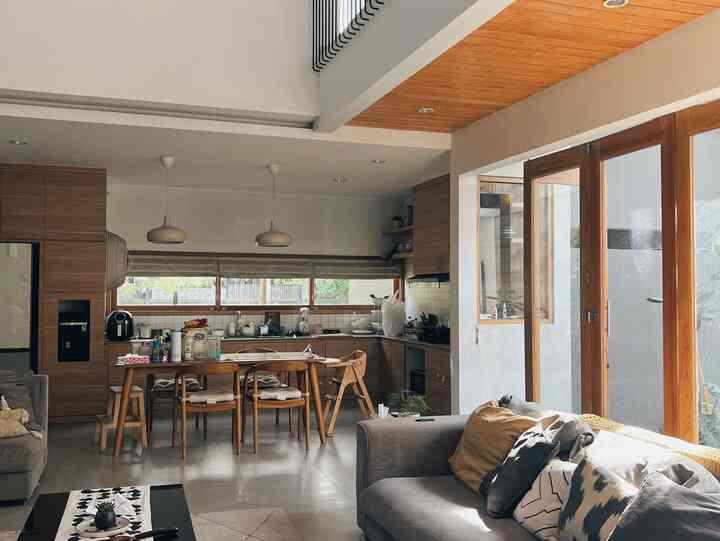 Natural modern dining and living room in warm beige and brown tones, featuring large windows with natural light and a baby high chair