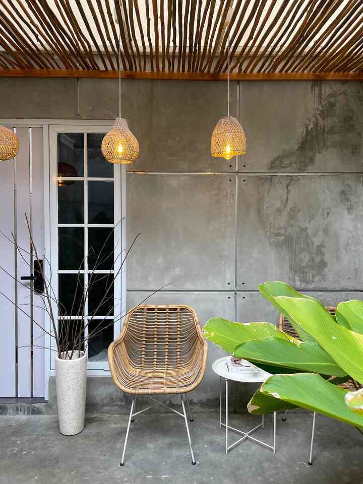 Wood tone and gray concrete wall terrace featuring rattan chairs and pendant lights with a cozy, warm atmosphere.