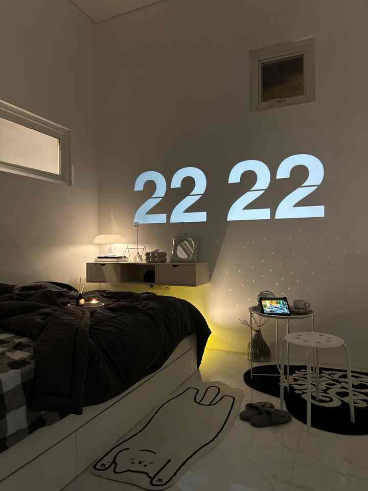 Modern and cozy bedroom with black bedding, white furniture, rugs, and a large projected clock on white walls