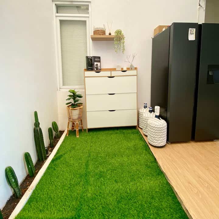 Natural wood and white shoe cabinet in a narrow veranda with green artificial grass flooring and plants in a minimalist setting