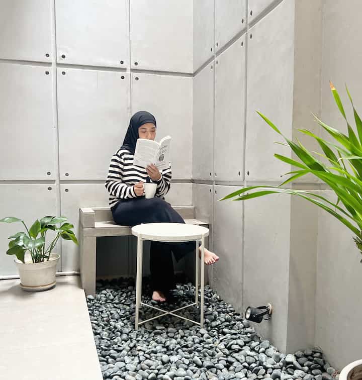 A small terrace space with gray concrete walls and a white side table, featuring a person reading a book in a modern, minimalistic atmosphere