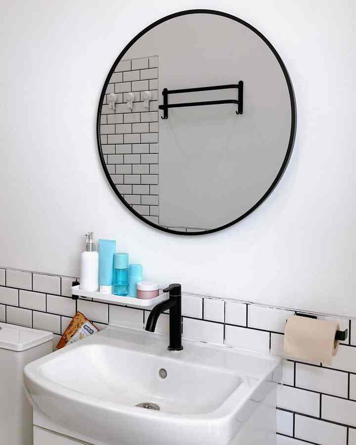 White and black toned bathroom featuring a black round mirror and faucet in a clean, minimalist space