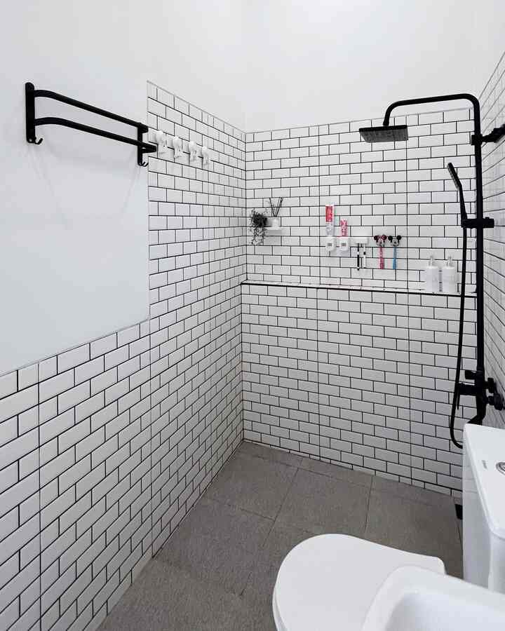 Monotone white and black bathroom featuring white tiled walls, black shower set, and towel rack with clean and modern aesthetic