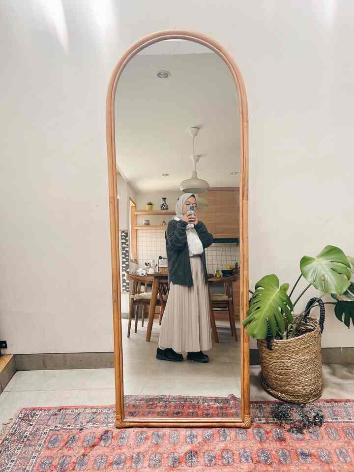 Natural wood tone and beige-toned entrance featuring a large rattan-framed standing mirror and a plant in a woven basket, creating a cozy atmosphere