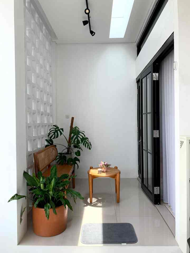 Bright natural balcony featuring white walls and floor, wooden bench and round wooden table, terracotta pot and green plants