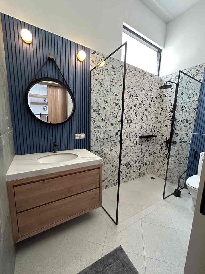 Natural-toned bathroom with terrazzo walls and blue panels, featuring a wood-tone vanity and simple design sink area