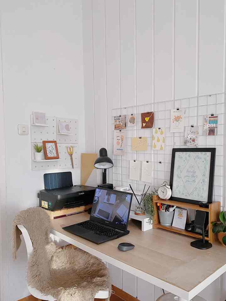 White tone home office featuring a large desk, black laptop, and peg board creating a clean and cozy workspace