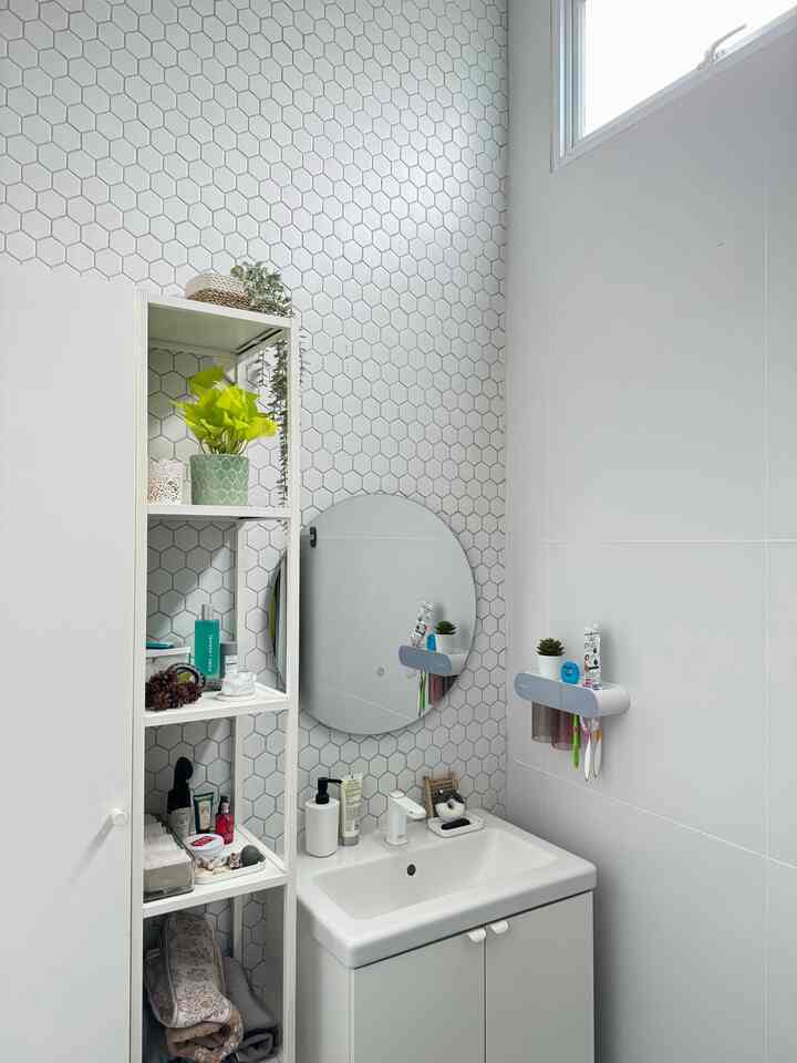 Bright white bathroom featuring a round mirror, white sink cabinet, hexagon tiled wall, and open shelving for storage in a clean space