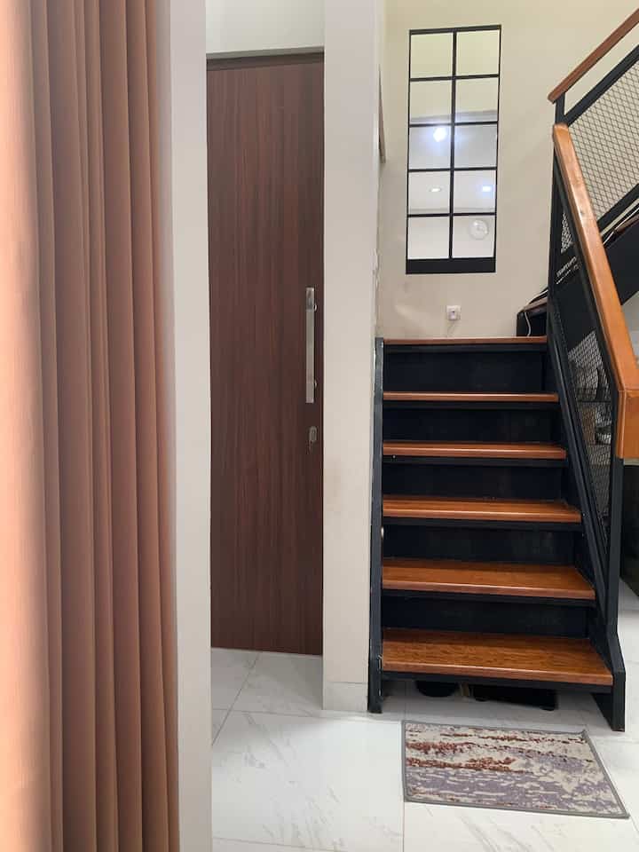 White and brown toned entrance space featuring wooden stairs, large grid-style mirror on wall, and an anti-slip mat creating a clean entry area