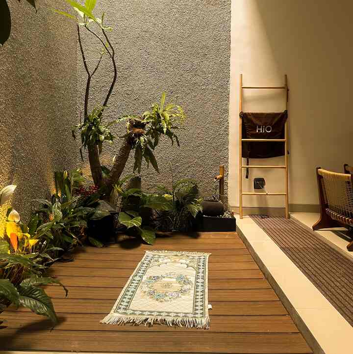 Warm wood tone veranda featuring lush plants and a small prayer rug, creating a practical and cozy multipurpose space