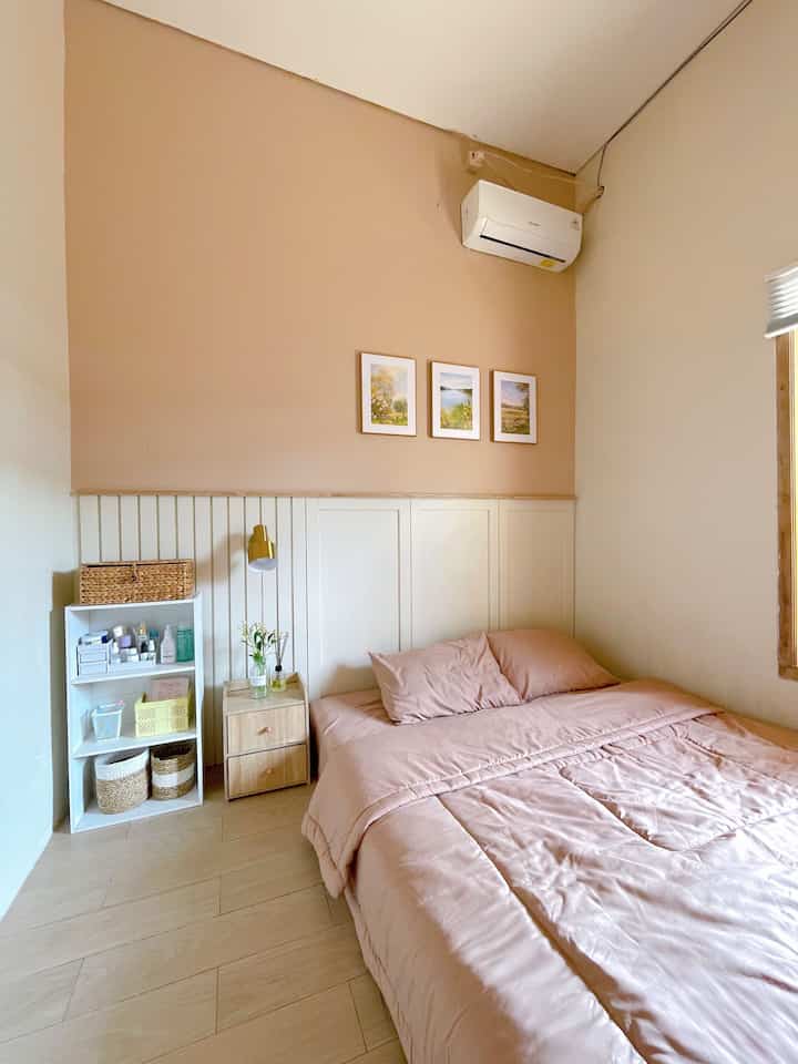 A cozy bedroom with warm beige and natural wood tones, featuring pink bedding, a wooden nightstand, and wooden framed wall art creating a comfortable atmosphere.