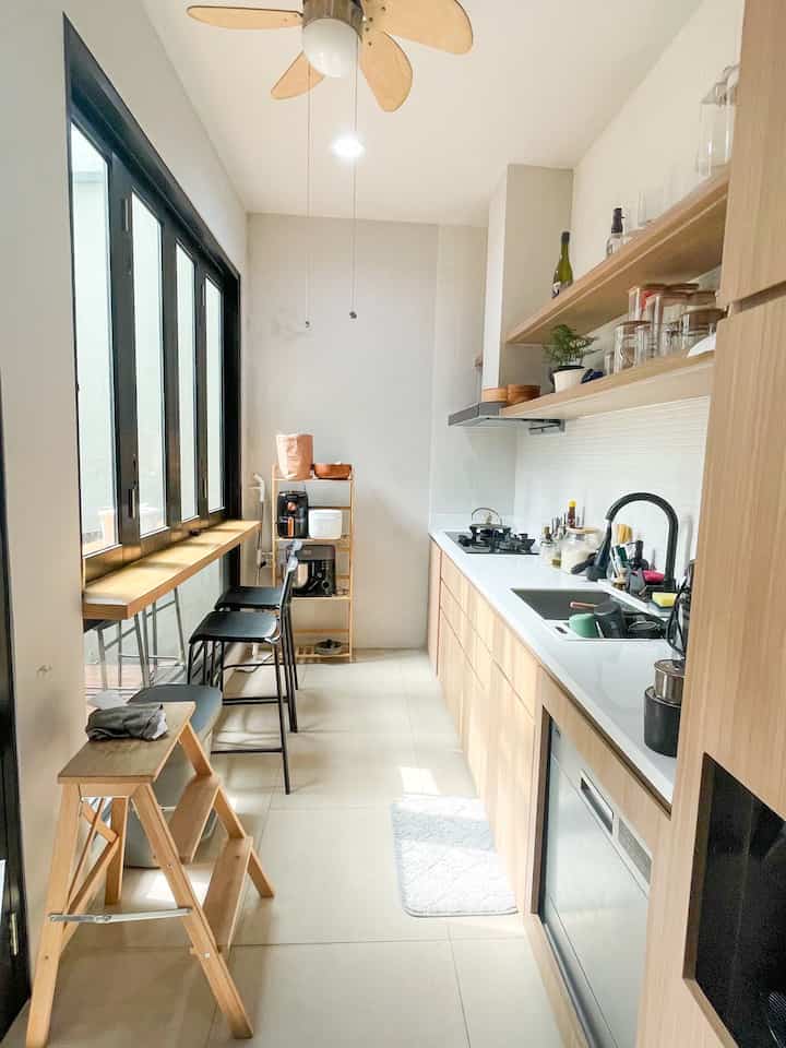 White and wood tone compact narrow kitchen featuring bar stools, shelving, and built-in dishwasher with clean look