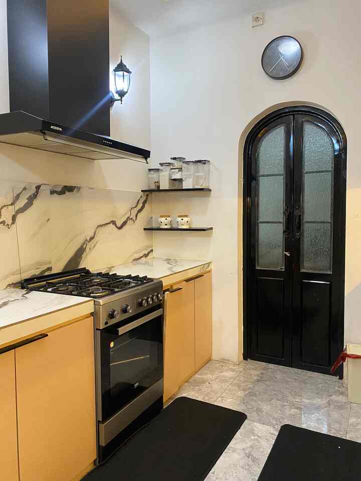 Compact kitchen in black and beige tones featuring stainless steel cooktop, marble-patterned backsplash, and wall clock for a practical setting