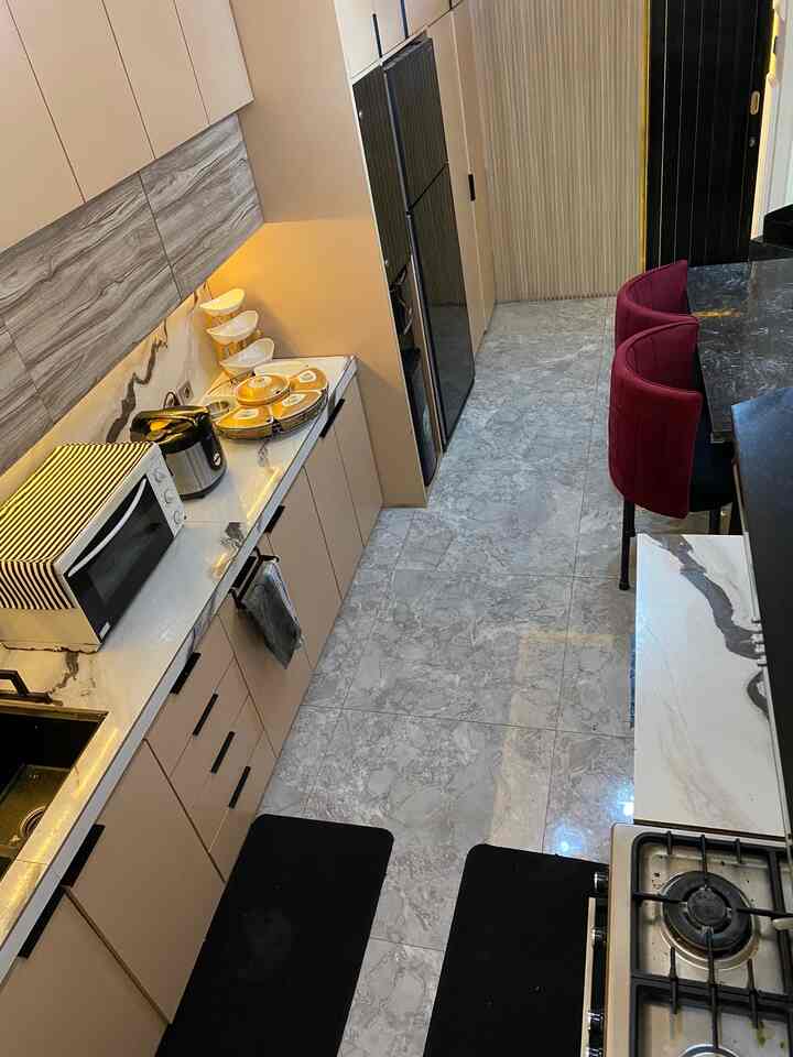 Beige and white toned long narrow modern kitchen featuring marble countertops and red dining chairs