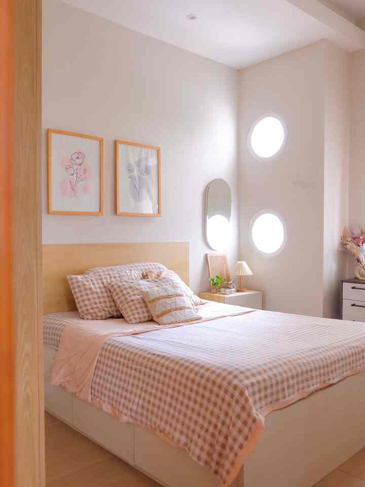 Soft wood tones and white walls blend in a bedroom featuring a queen-size bed, nightstand, and round windows, creating a cozy and simple atmosphere