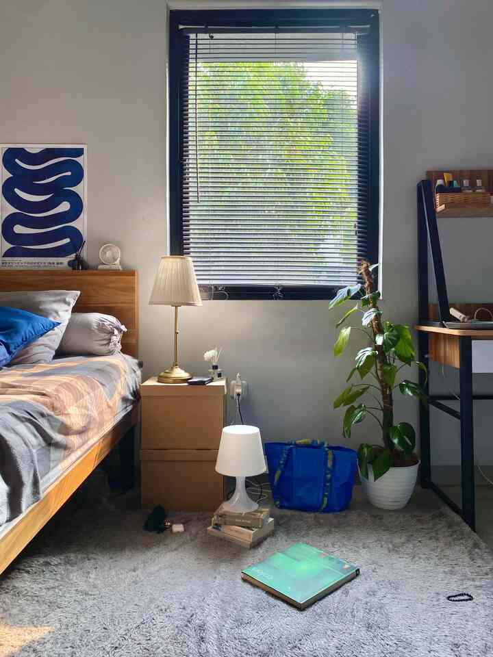 Light gray rug and wood-tone furniture furnish a mid-century modern style bedroom featuring table lamps and a large plant creating a cozy atmosphere