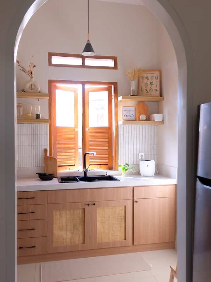 White and wood tone kitchen featuring a black sink under the window with shelves on either side, presenting a warm and clean atmosphere