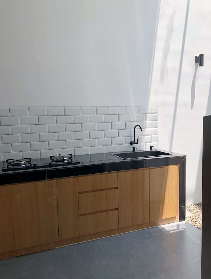 Minimalist L-shaped kitchen in white and brown tones, featuring clean cabinets and a subway tile backsplash with a sleek black sink