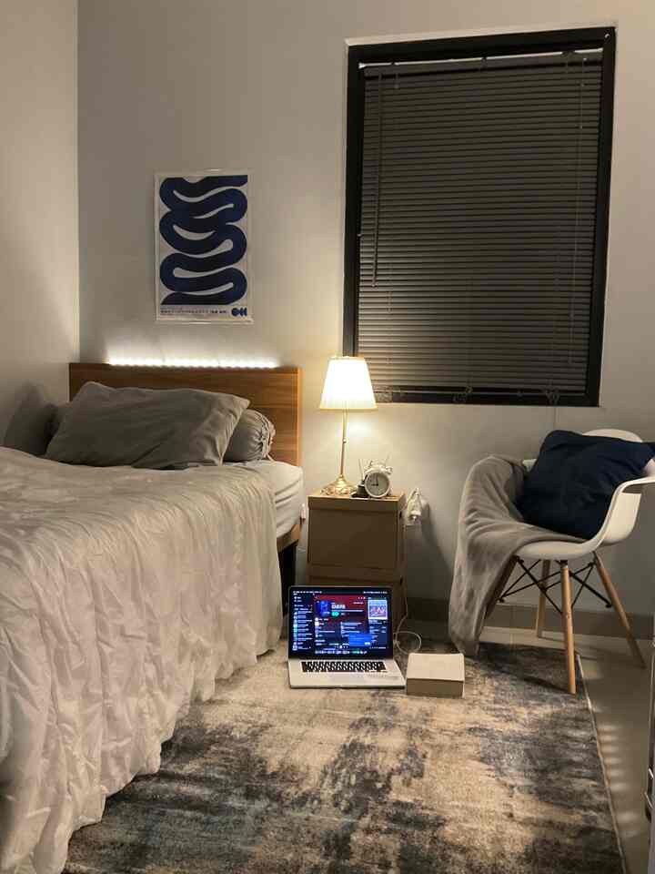 Bright white and gray toned bedroom featuring wooden bed frame, side table, laptop and lamp in a cozy setup