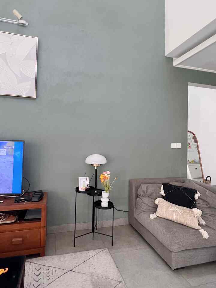 Living room with muted green wall featuring dark gray sofa, table lamp, and vase on decorative plant stand