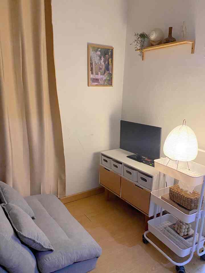 White-walled living room with brown flooring, featuring a sofa bed and Akari-style floor lamp creating a warm and minimal atmosphere