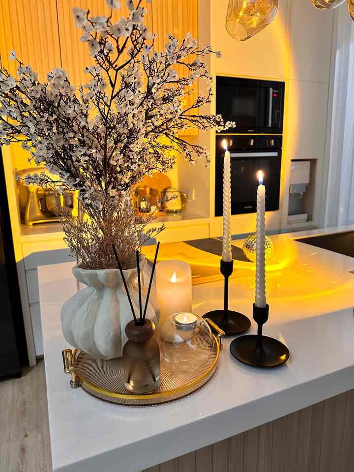 White kitchen with warm gold lighting featuring a blooming vase and candles arranged elegantly on the island countertop
