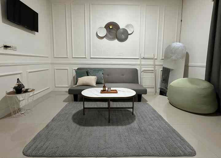 Minimalist compact living room with a gray sofa and white coffee table centered on a large gray carpet