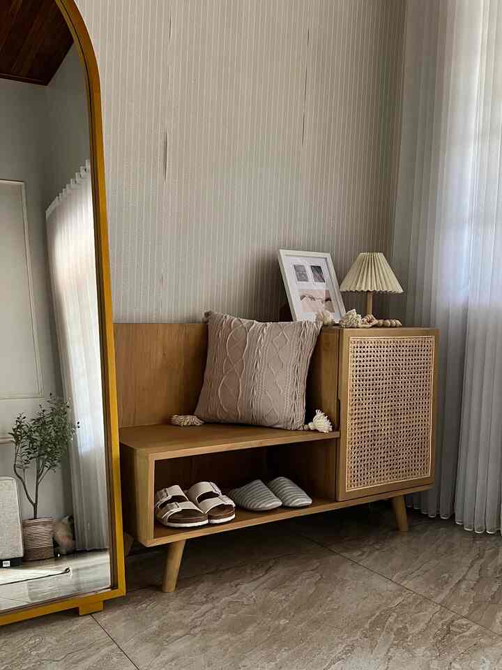 Beige and wood tone entrance space featuring a knit cushion and a table lamp on a wooden bench, creating a cozy atmosphere