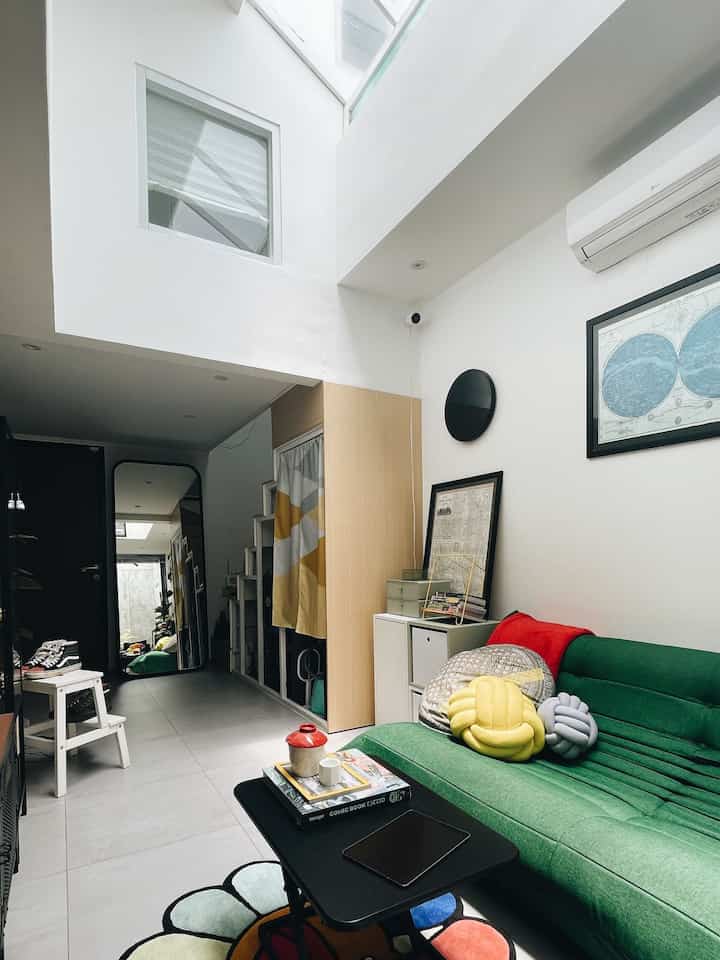 Bright white and natural wood narrow living room featuring green sofa, coffee table, colorful cushions and a flower-shaped rug